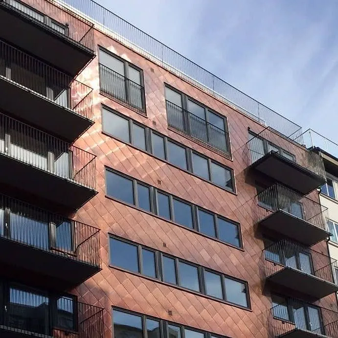 Fasade på moderne bygg med kobberfarget kledning og flere sorte balkonger.