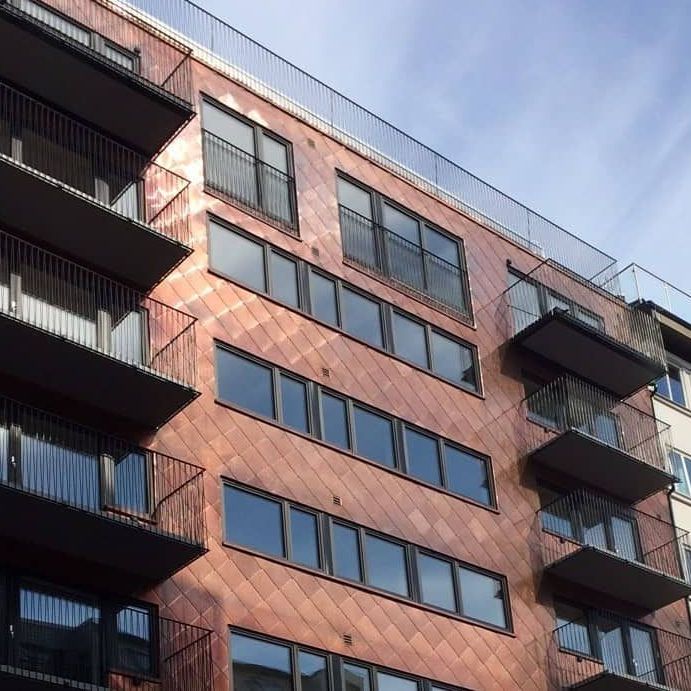 Fasade på moderne bygg med kobberfarget kledning og flere sorte balkonger.