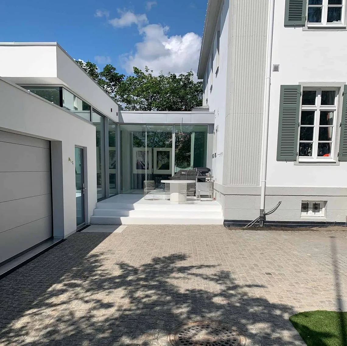 Moderne tilbygg med glassfasader forbinder garasje og hovedbygning i eksklusivt uteområde.