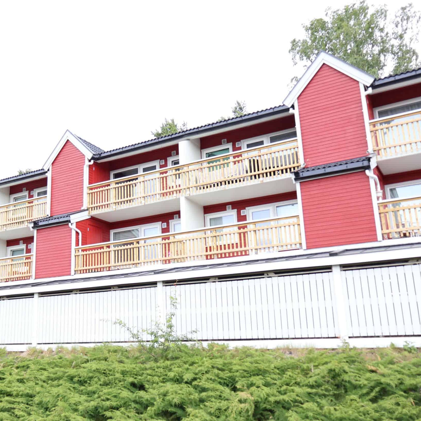 Leilighetsbygg med rød trekledning og romslige balkonger i skrånende terreng.