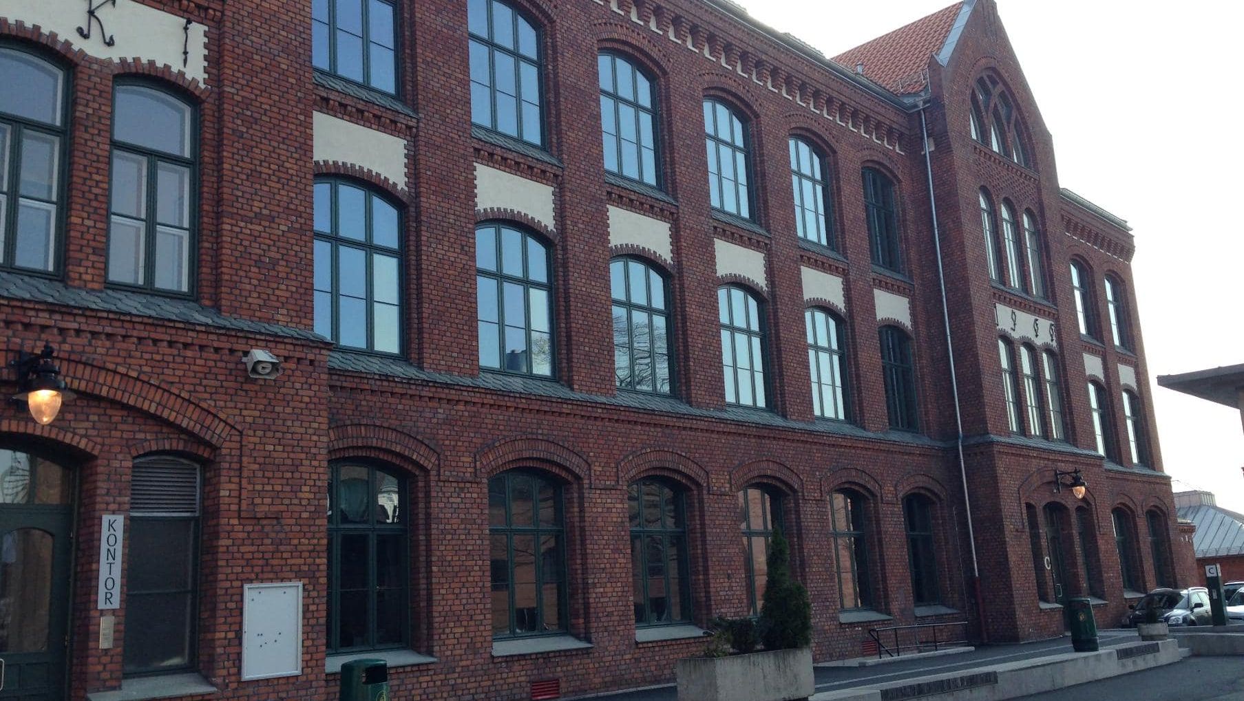 Fasade av en stor mursteinsbygning i tre etasjer med mange bueformede vinduer.