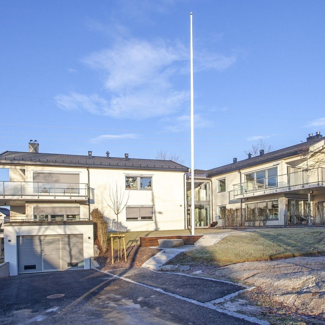 Boligkompleks med lyse fasader, balkonger og felles uteområde rundt sentral flaggstang.