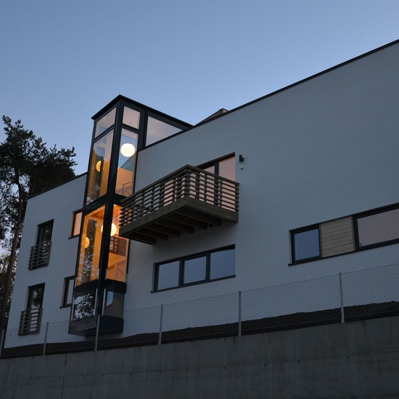 Moderne hus ved kveldstid med opplyste vinduer og glassheis.