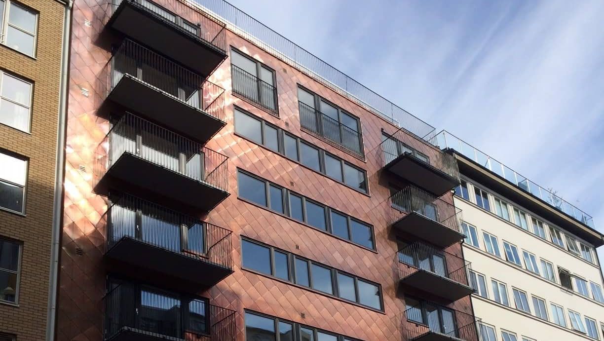 Fasade på moderne bygg med kobberfarget kledning og flere sorte balkonger.