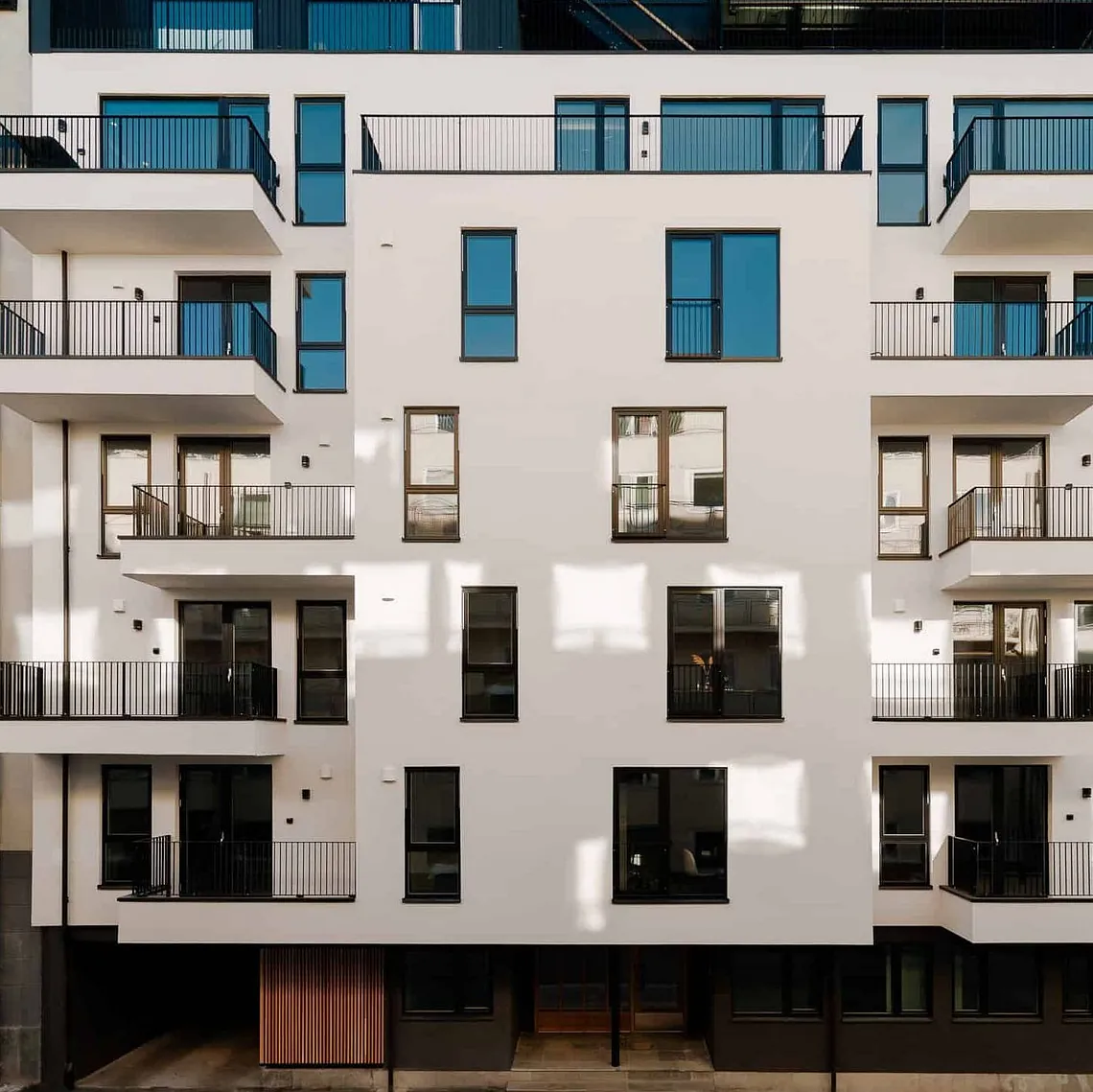 Nybygd leilighetsbygg med balkonger og store vinduer, omgitt av eldre bygårder.