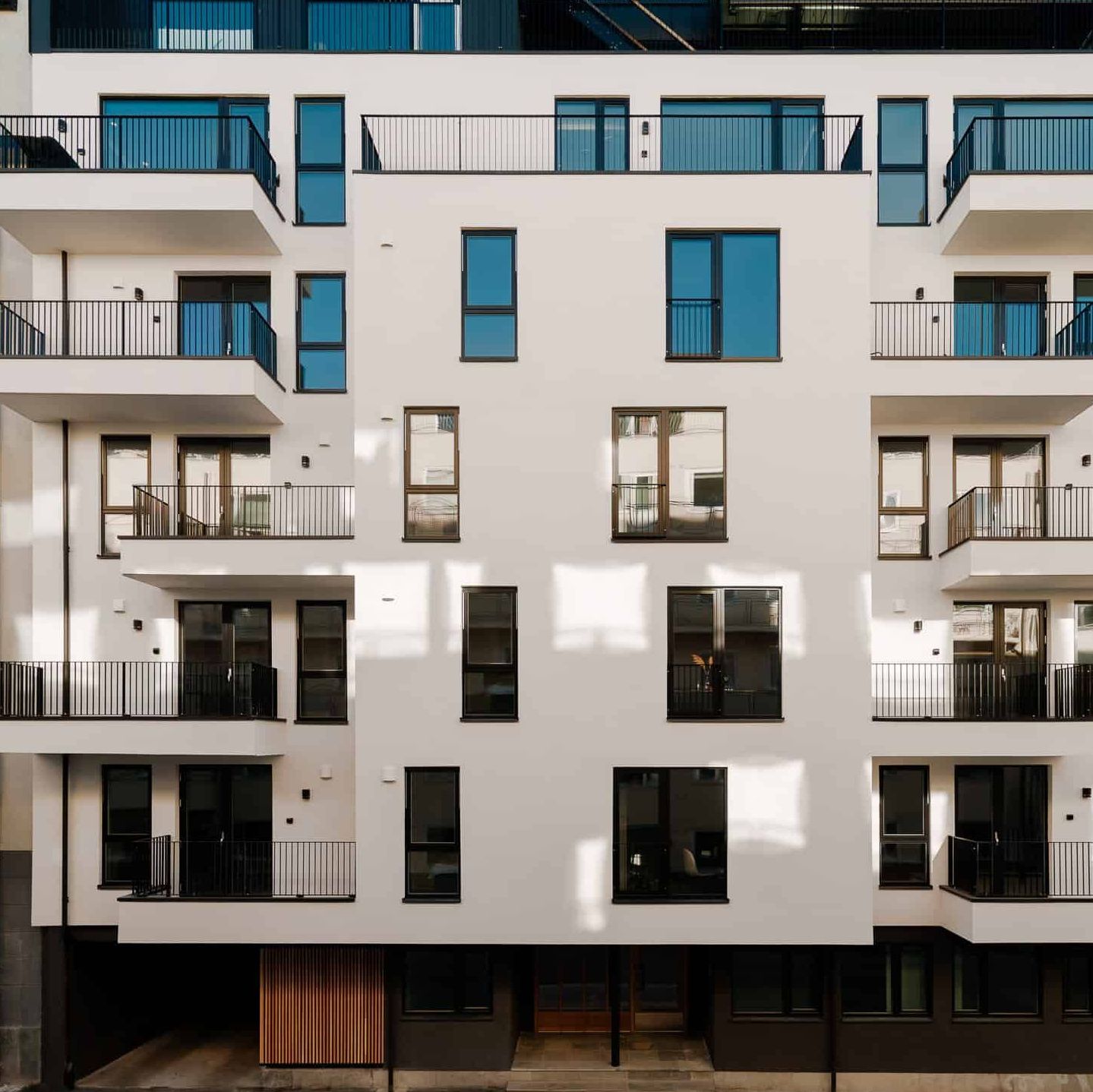 Nybygd leilighetsbygg med balkonger og store vinduer, omgitt av eldre bygårder.