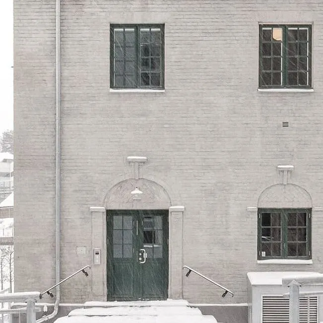 Murbygning i snødekt landskap med grønn dør og små vinduer.
