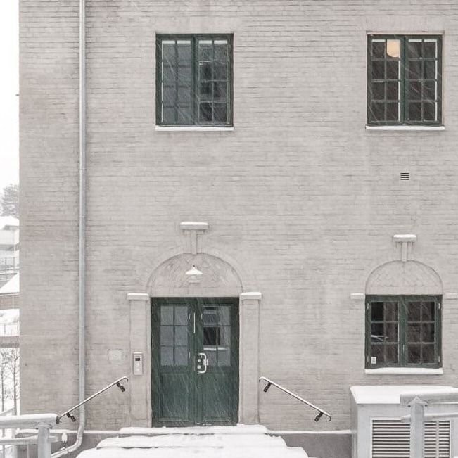 Murbygning i snødekt landskap med grønn dør og små vinduer.