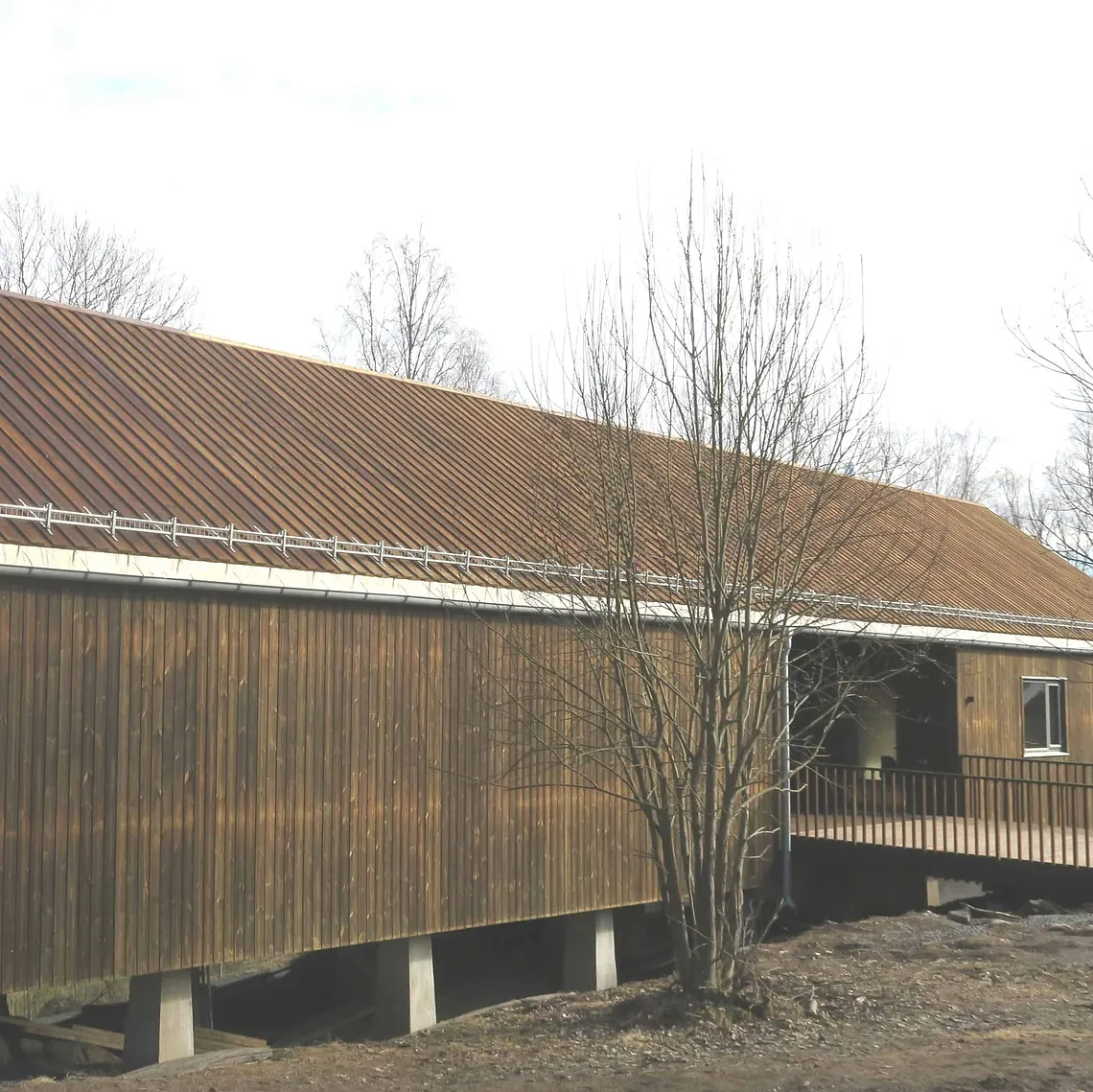 Bygning med trekledning og metalltak er oppført på søyler i naturnært og skrånende terreng.